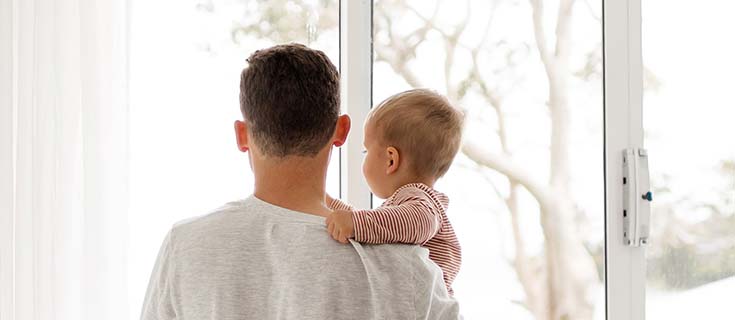 Père tenant son bébé dans les bras en regardant par la fenêtre
